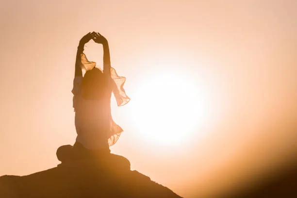 A person sitting cross legged in meditation against a sunset sky