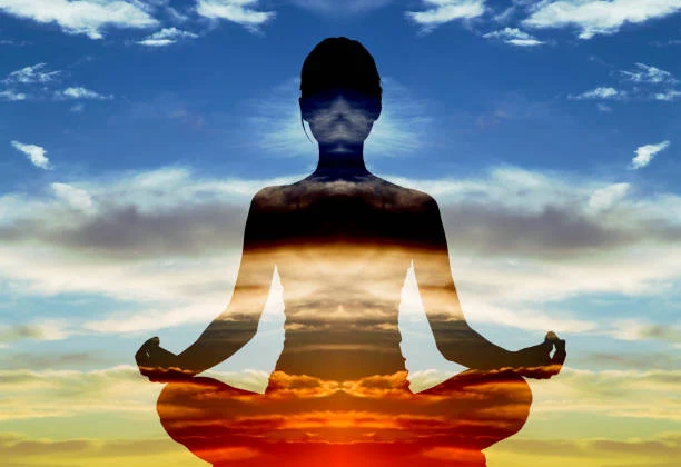 A silhouette meditating in a lotus position against sky and water