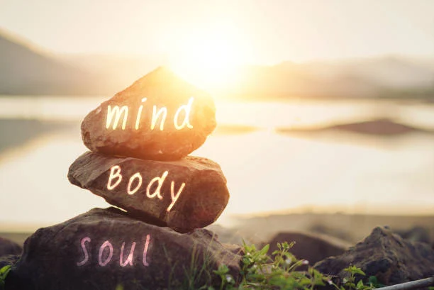 Stones stacked at the water edge painted with the words mind, body and soul