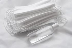 A stack of disposable face masks beside a bottle of hand sanitiser