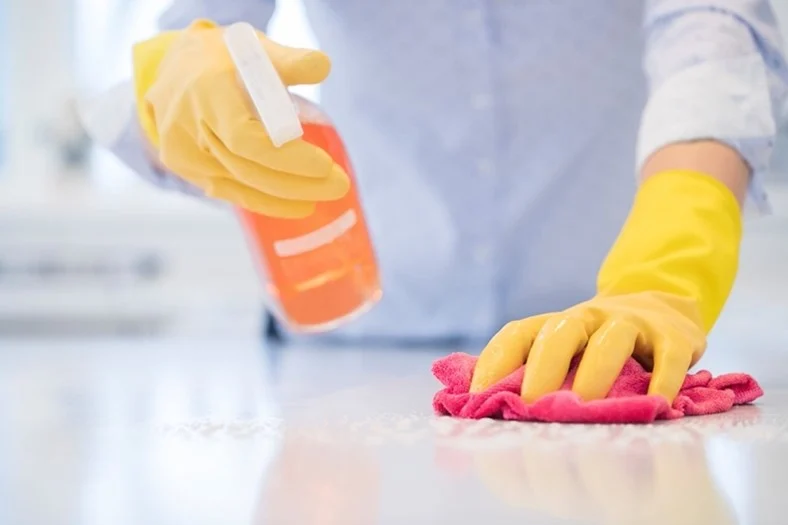 A gloved hand holding a spray bottle while cleaning a surface