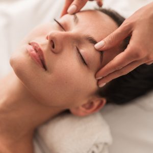 From above calm female closing eyes and enjoying face massage during session in spa salon