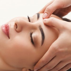 Woman enjoying anti aging facial massage. Pretty girl getting professional skin care at wellness center. Relaxation, beauty, spa and face treatment concept, copy space